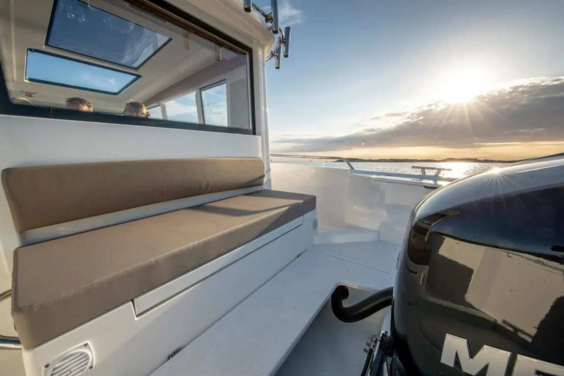 A modern boat's interior featuring a cushioned bench, a sleek engine, and a sunset view through large windows.